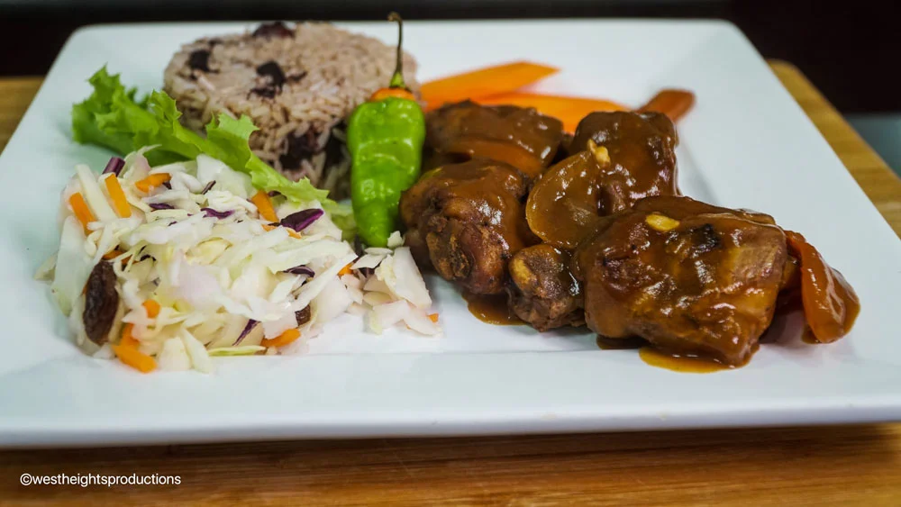 Inviting image showcasing the culinary excellence of Jerk and BBQ Haven, the premier destination for the best jerk chicken in Mississauga. The photograph captures a delectable Stew Chicken Dinner, accompanied by fragrant Rice & Peas and a fresh Salad.