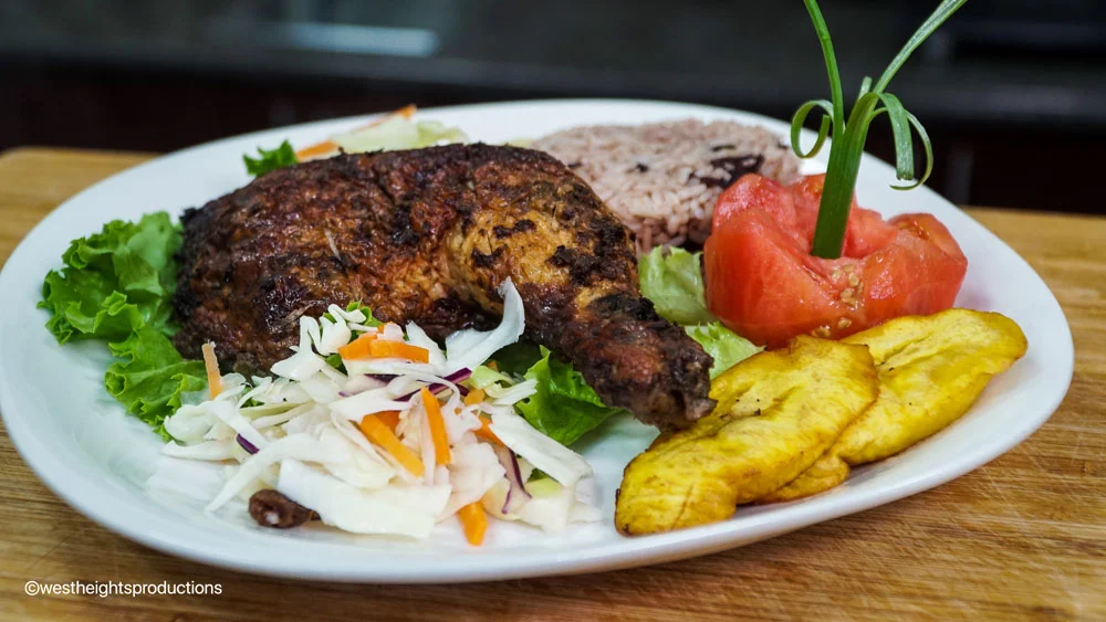 A tantalizing image showcasing the expertise of Jerk and BBQ Haven, a top-notch establishment renowned for its mouthwatering jerk chicken in Mississauga. The photograph highlights a scrumptious Jerk Chicken Dinner, served with aromatic Rice & Peas, perfectly cooked Plantains, and a refreshing Salad.
